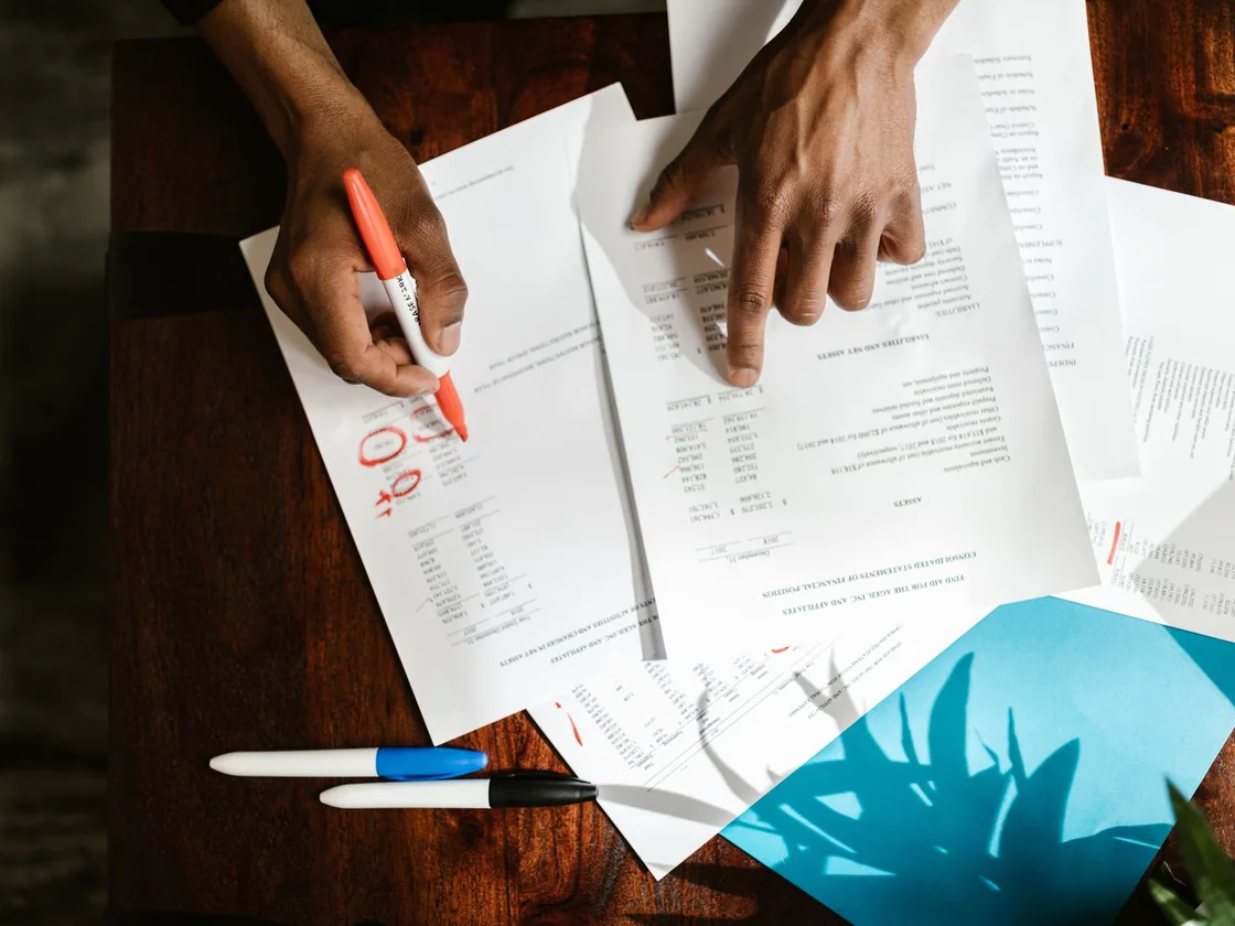 Hands circling numbers on a stack of printed financial statements with a red marker