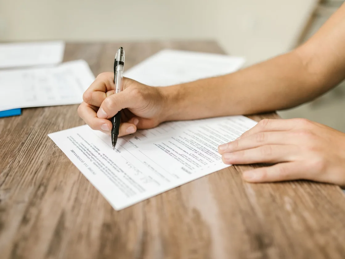 A homeowner filling out a seller disclosure form with a pen at a wooden kitchen table