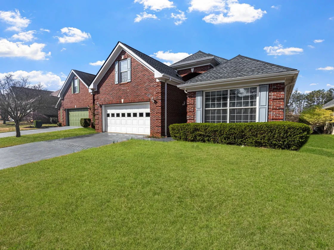 A red brick suburban house with a gabled roof and attached garage on an ordinary metro Atlanta street