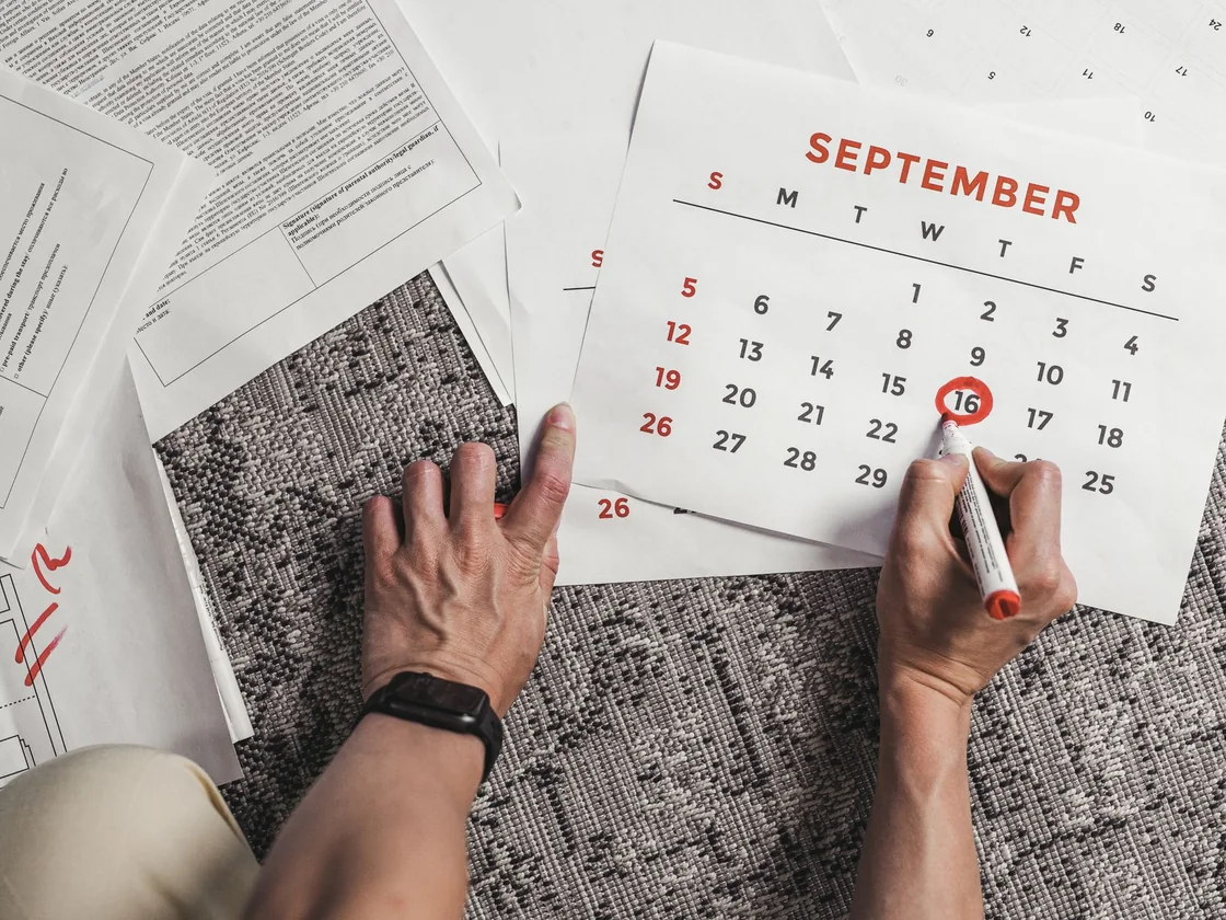 Hands circling a date in red on a paper calendar surrounded by official documents
