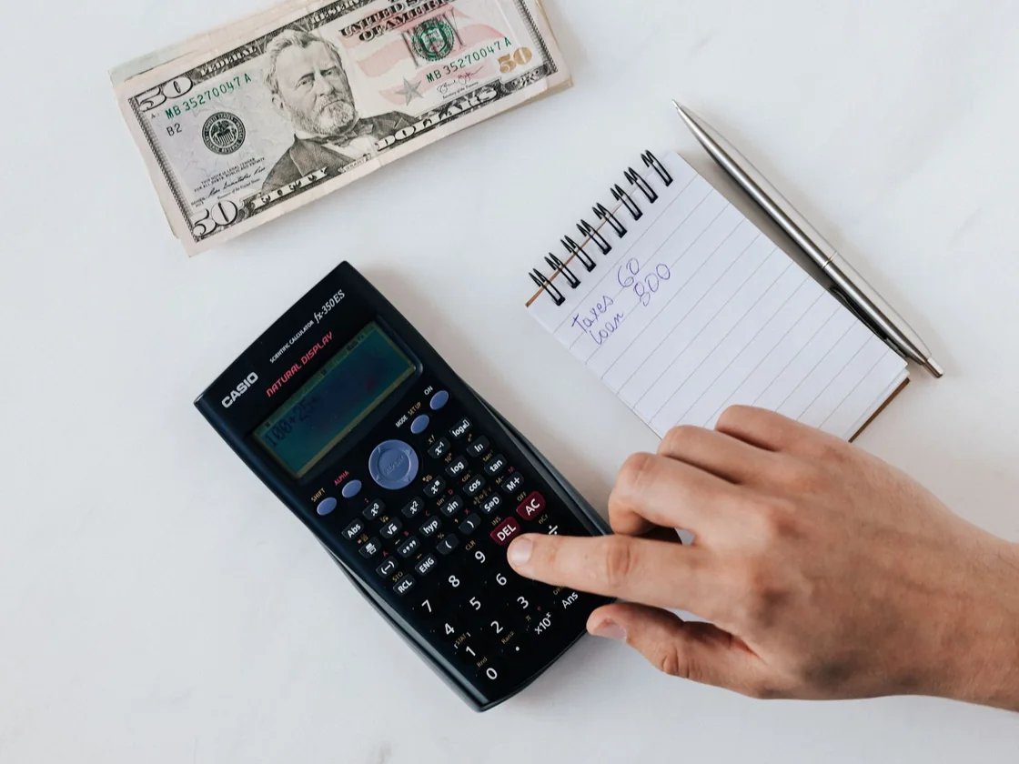 A calculator, a notepad with a figure written on it and cash on a table while someone works out what a house sale will net