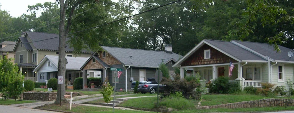 A row of modest craftsman bungalows with deep porches and shaded front yards on an ordinary residential street in the Atlanta area