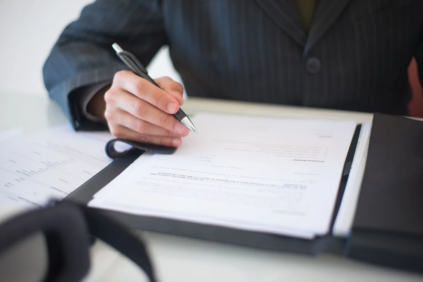A seller signing the closing package at a desk, the stack of pages where every cost of the sale is listed