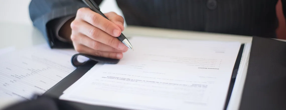 A seller signing the closing package at a desk, the stack of pages where every cost of the sale is listed