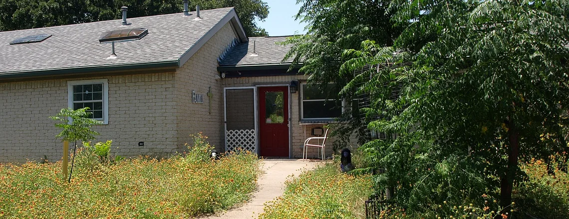 A dated one-story brick ranch house with an overgrown front yard on an ordinary street in Arlington, Texas, in the Dallas area