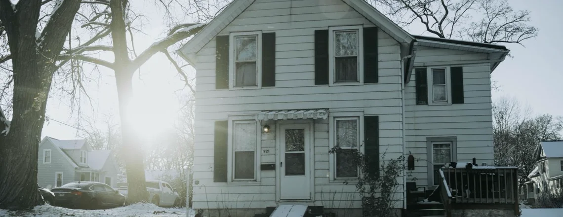 A modest older single-family house on an ordinary Detroit street in winter, the kind sold as-is
