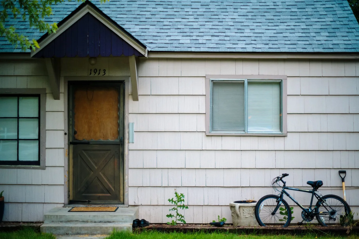 A small house with faded shingle siding and a worn wooden screen door on an ordinary street
