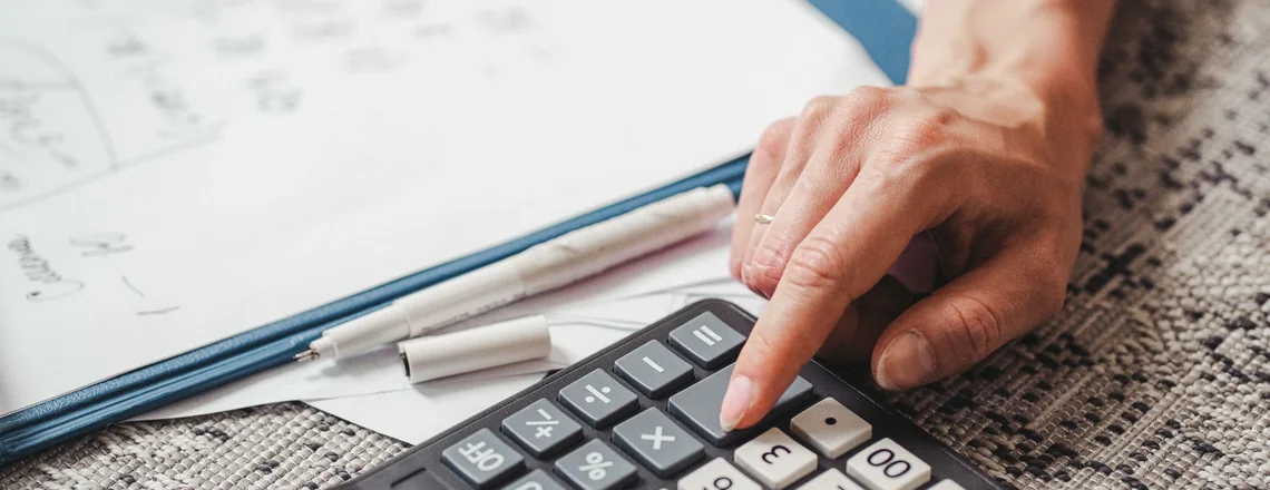 A hand working out a loan payoff figure on a desk calculator next to handwritten notes