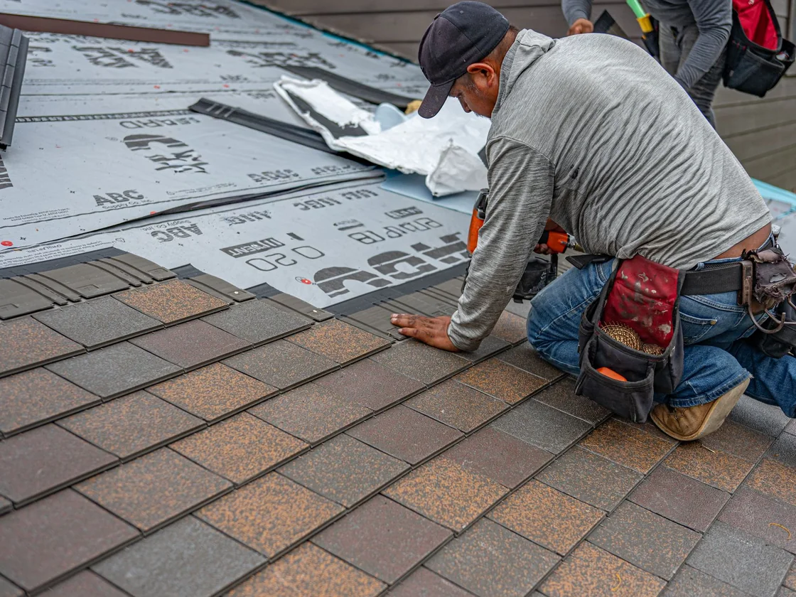 A roofer nailing down new asphalt shingles on an ordinary house, the job a Florida insurer may force before it writes a policy