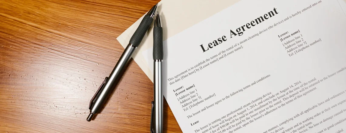 A signed lease agreement and two pens on a wooden desk