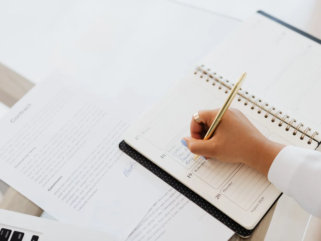 A hand writing a closing date into a week planner next to the signed contract on a desk