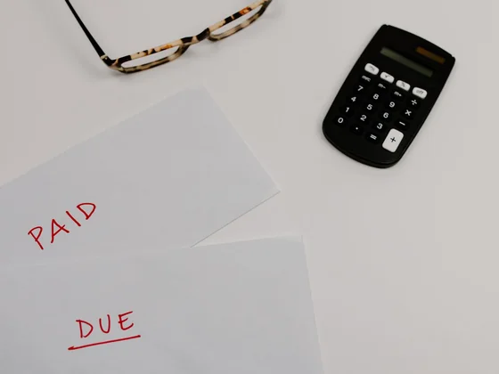 An overdue property tax notice and bills on a kitchen table with a calculator and reading glasses