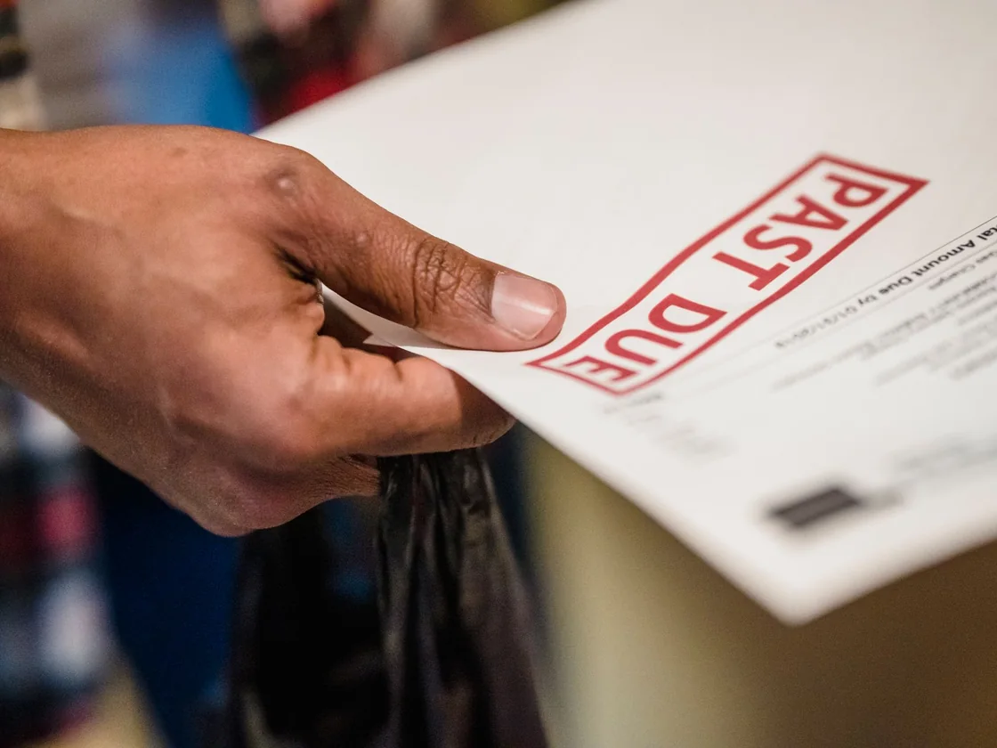 A hand holding a bill stamped past due in red, the kind of notice that arrives after a missed property tax deadline