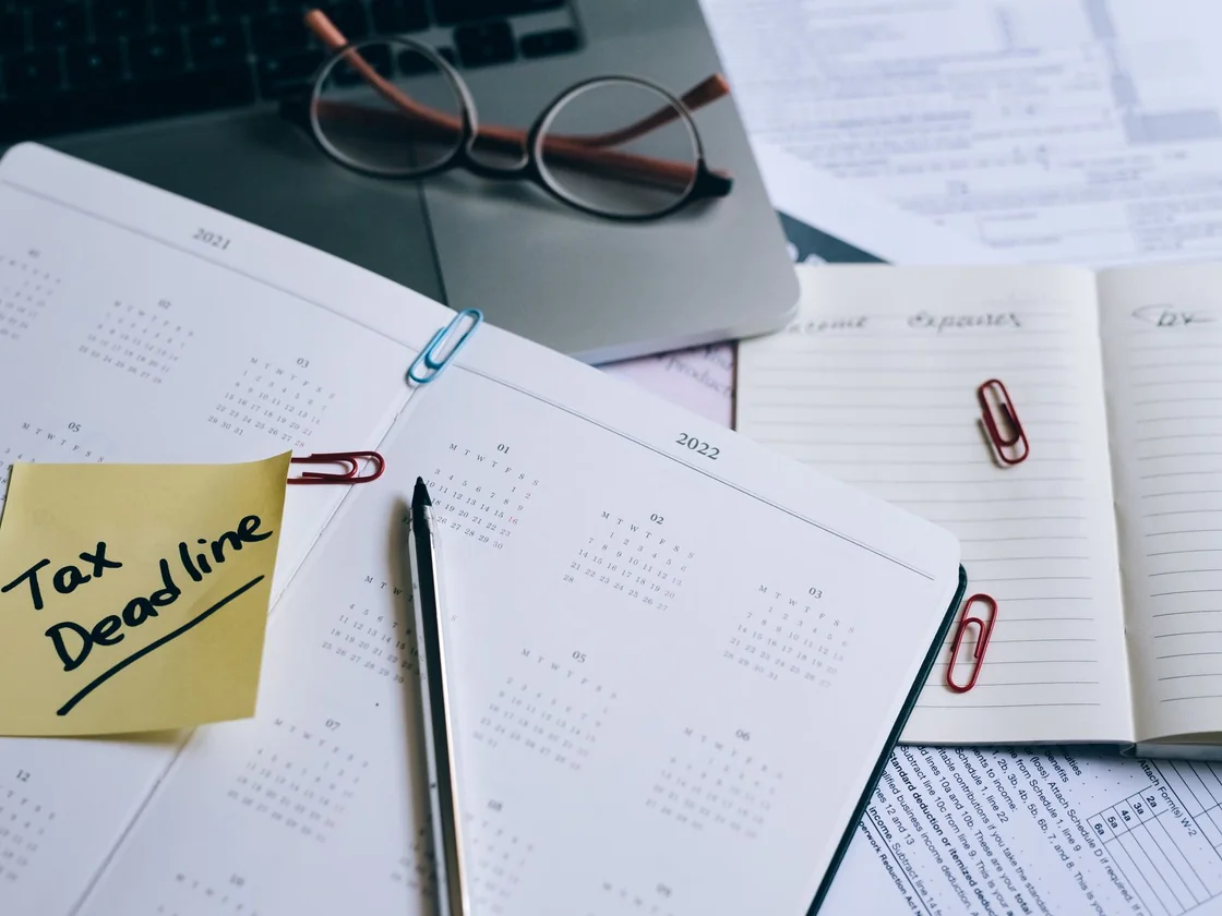 A desk planner with a sticky note reading tax deadline beside tax paperwork