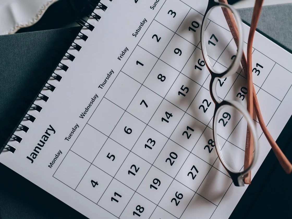 A desk calendar showing a full month with a pair of reading glasses resting on the page