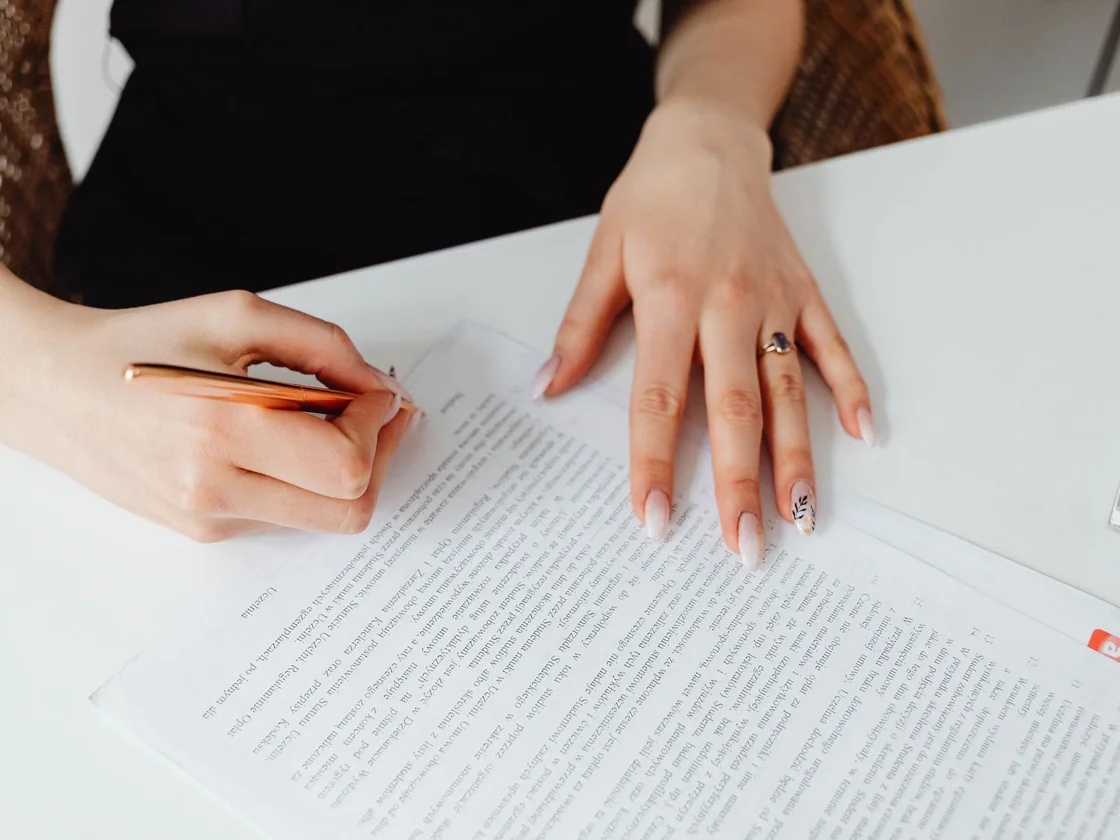 A person signing an official document at a desk with a pen and a signature tab on the page