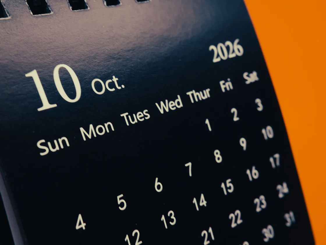 A desk calendar page open on October 2026 against a plain orange background