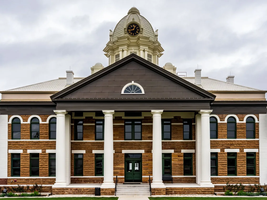 A Texas county courthouse with stone columns and front steps under a grey sky