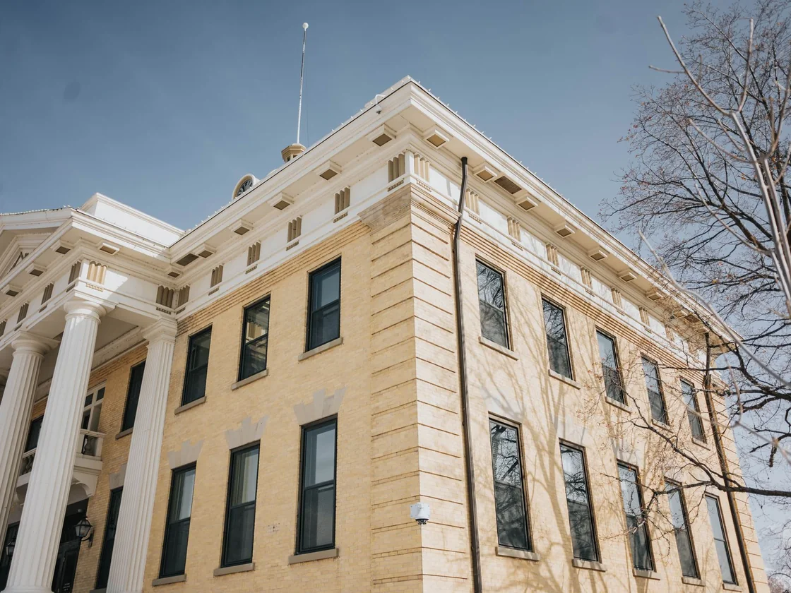 A stone county courthouse with tall columns photographed from below against a clear sky