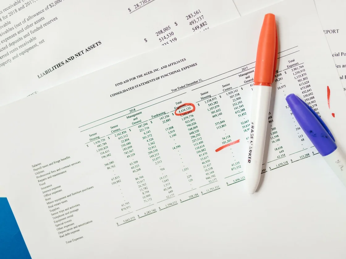 Financial statements on a desk with one figure circled in red and two marker pens