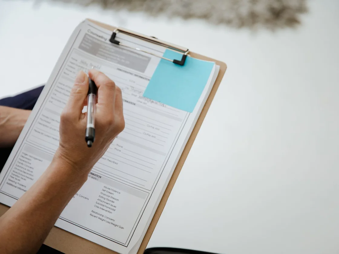 A hand filling in a printed property disclosure form held on a clipboard